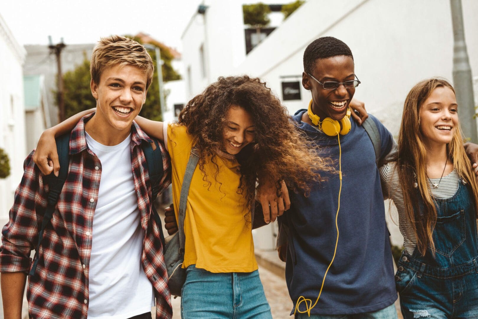 Teenage boys and girls walking in the street holding each other. Smiling college friends walking together in street wearing college bags having fun.