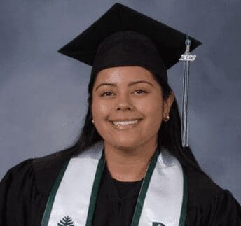 Smiling graduate wearing cap and gown with honor cords.