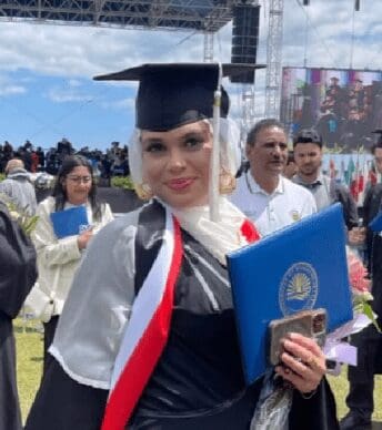 Graduate in cap and gown holding diploma with crowd behind.