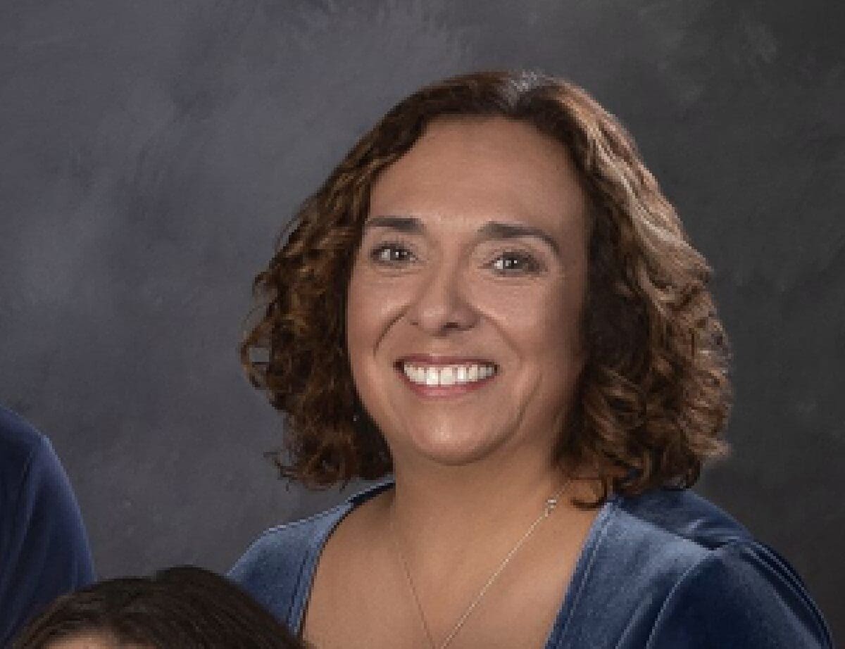 A smiling woman with curly hair against a gray backdrop.