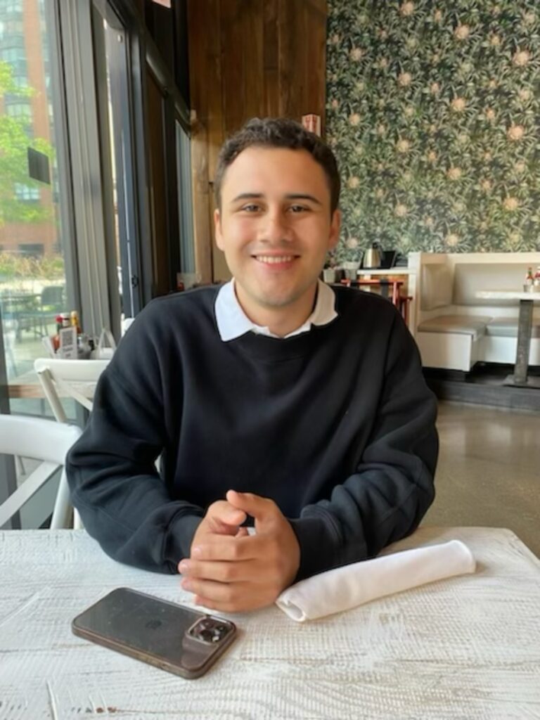 A young man smiling while seated at a restaurant table.