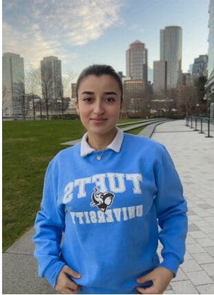 A person wearing a blue Tufts University sweatshirt in a city park.