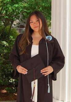 Young woman in graduation gown holding cap outdoors.