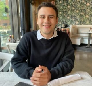 A young man smiling while seated at a restaurant table.