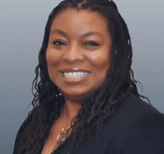 Professional headshot of a smiling woman with braided hair in business attire.