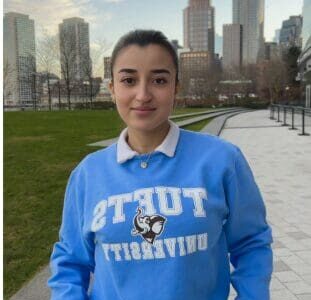 A person wearing a blue Tufts University sweatshirt in a city park.