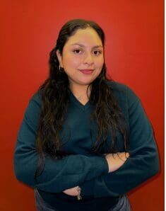 Young woman with long dark hair wearing a dark green sweater against a red background.